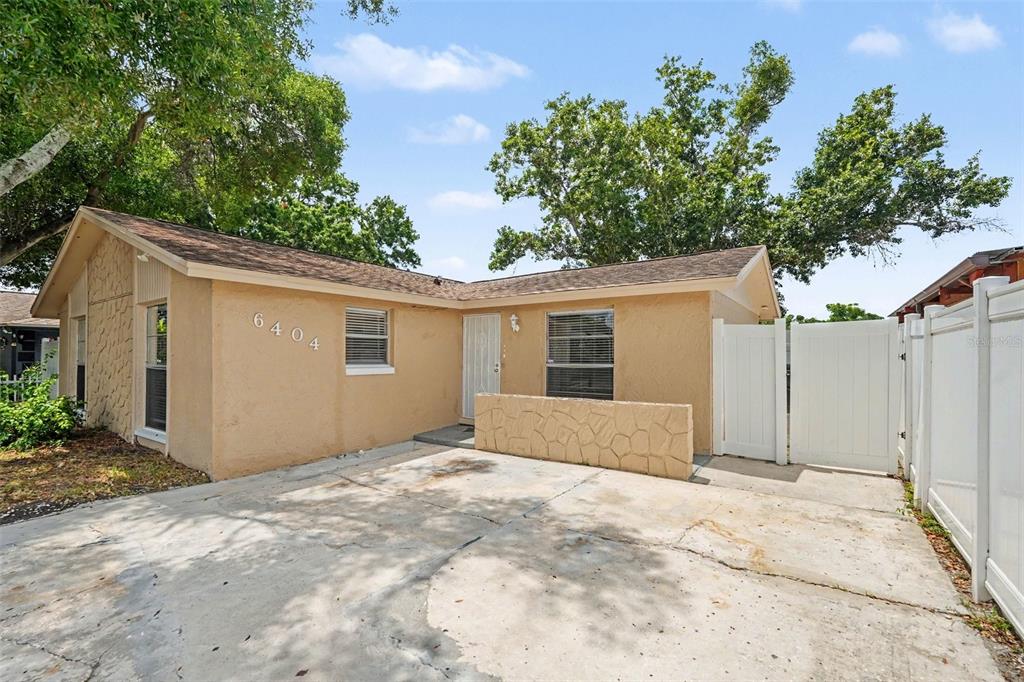 A single-story tan house with a concrete driveway, stone accents, and a white vinyl fence — 6404 FREEDOM COURT, TAMPA, FL