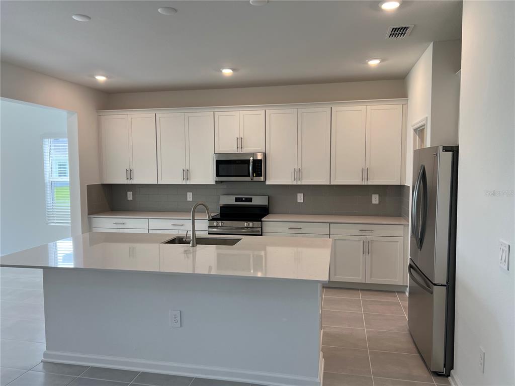 A modern kitchen features white cabinets, stainless steel appliances, a quartz island, and gray tile — 5511 NINA WAY, ST CLOUD, FL