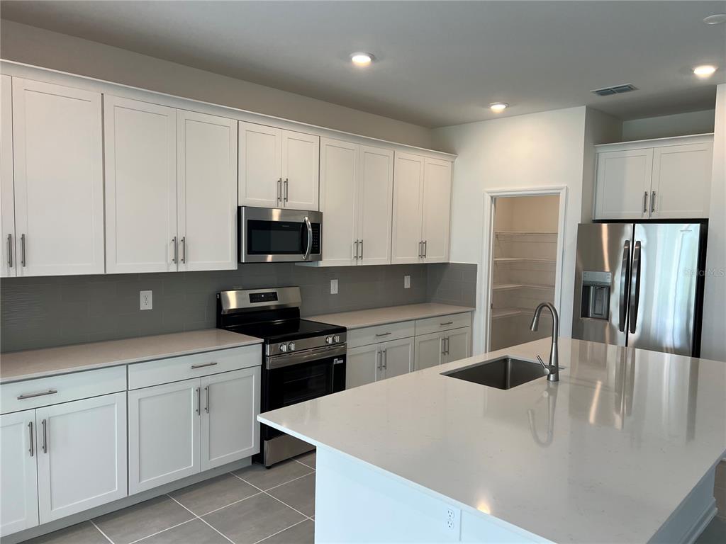 A modern kitchen features white cabinets, stainless steel appliances, a quartz island, and gray tile — 5511 NINA WAY, ST CLOUD, FL