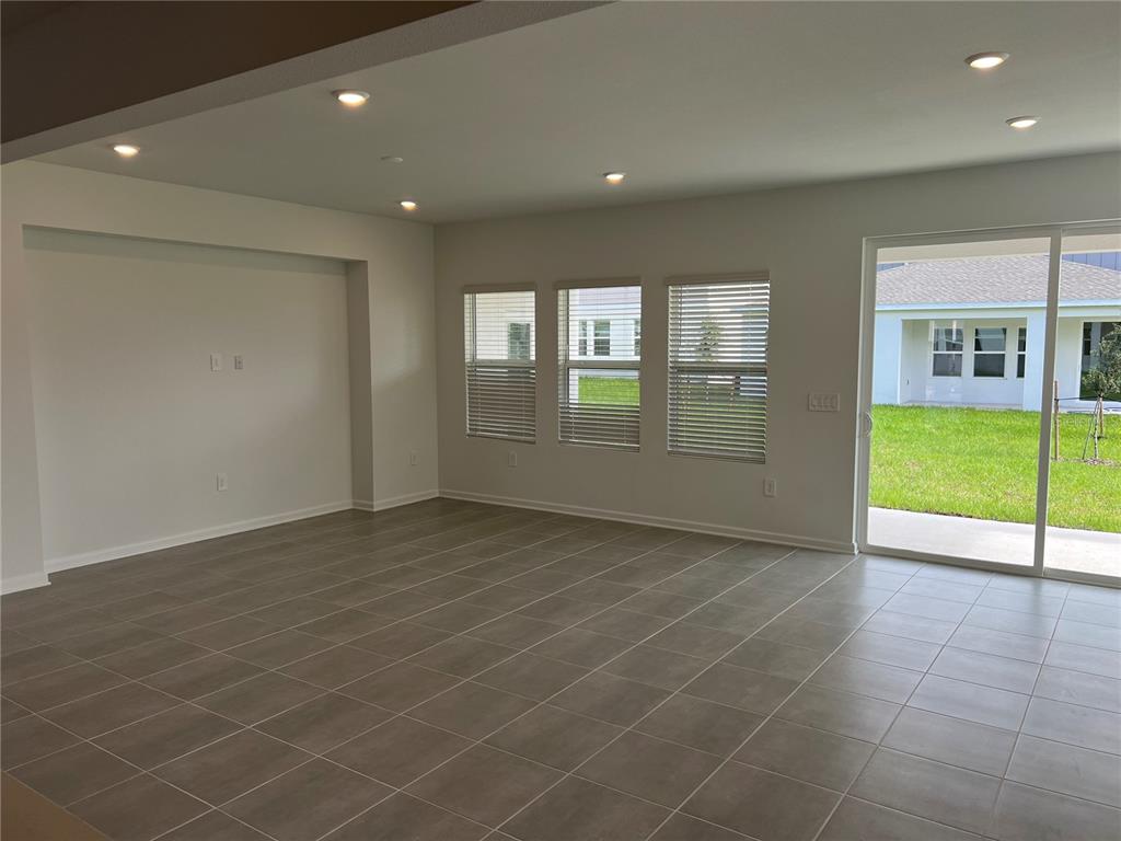 An empty living room features large tile flooring, recessed lighting, and a sliding glass door — 5511 NINA WAY, ST CLOUD, FL