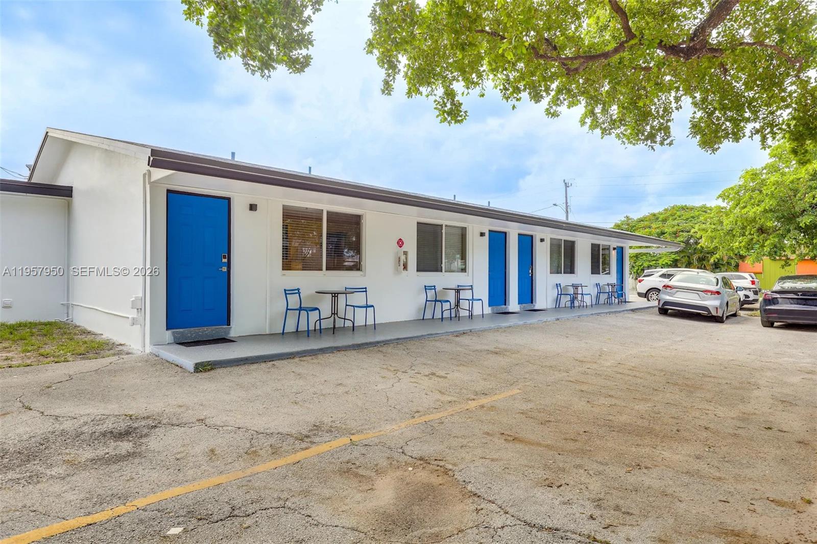 A single-story motel building features white exterior walls, blue doors, and small outdoor seating areas — 412 NE 4th Ave, Hallandale Beach FL 33009, HALLANDALE BEACH, FL