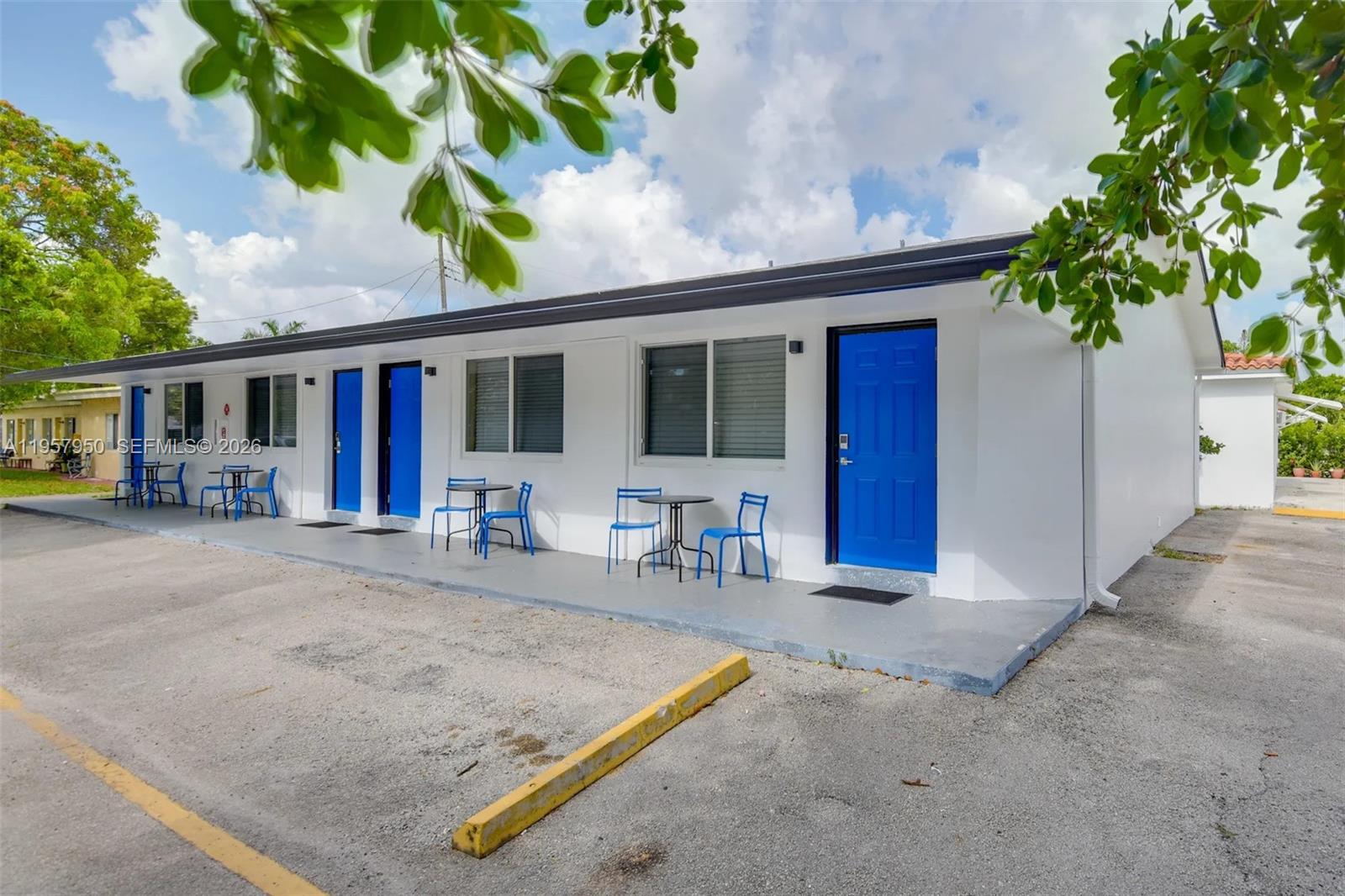 A single-story motel building features white exterior walls, blue doors, and outdoor seating areas — 412 NE 4th Ave, Hallandale Beach FL 33009, HALLANDALE BEACH, FL