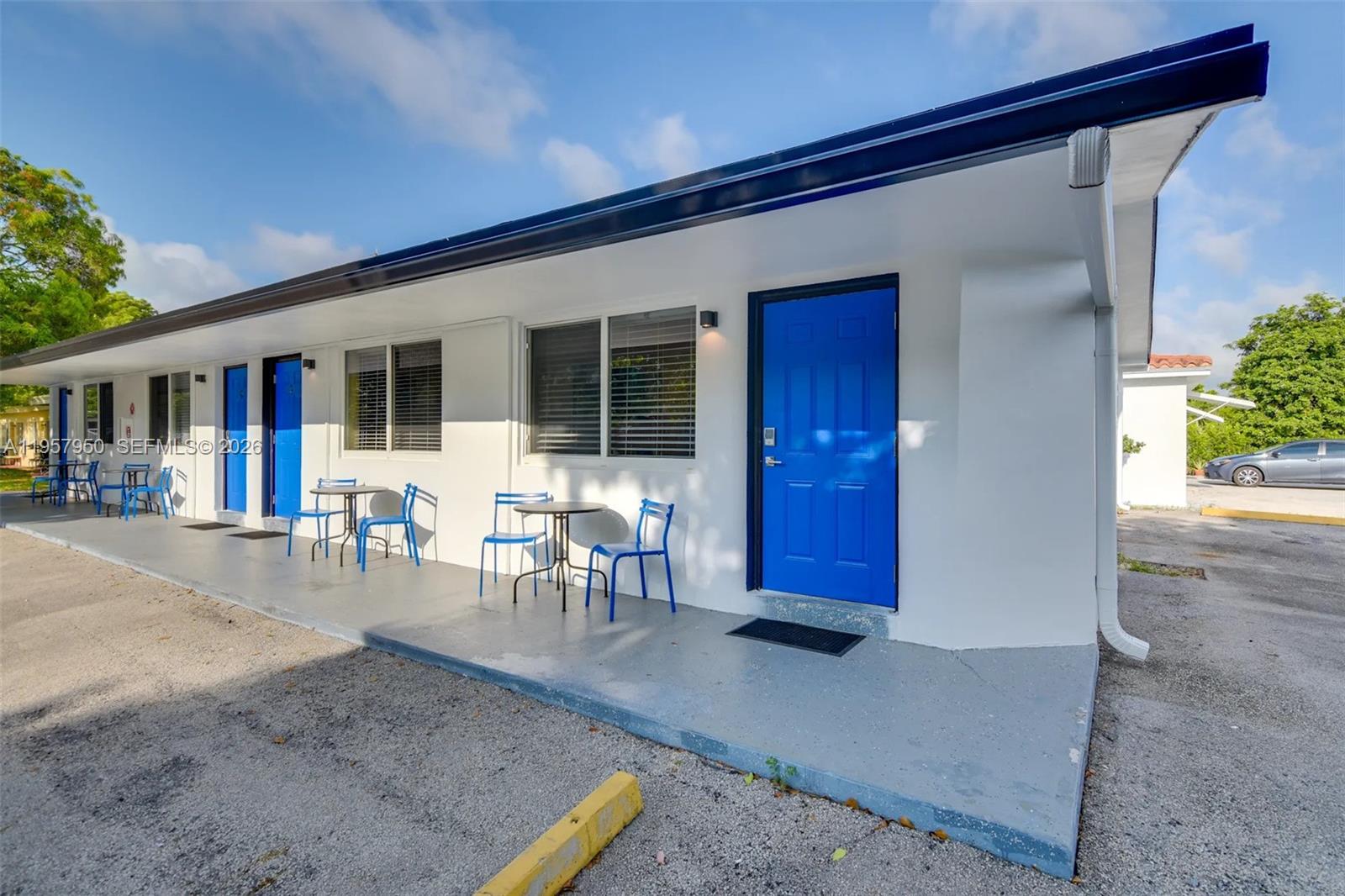 A row of motel-style rooms with blue doors, outdoor seating, and a concrete walkway — 412 NE 4th Ave, Hallandale Beach FL 33009, HALLANDALE BEACH, FL