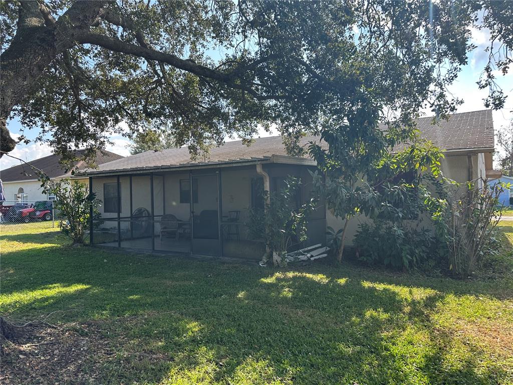 A screened-in patio is attached to the rear of a single-story house under large trees — 746 MADERIA COURT, KISSIMMEE, FL