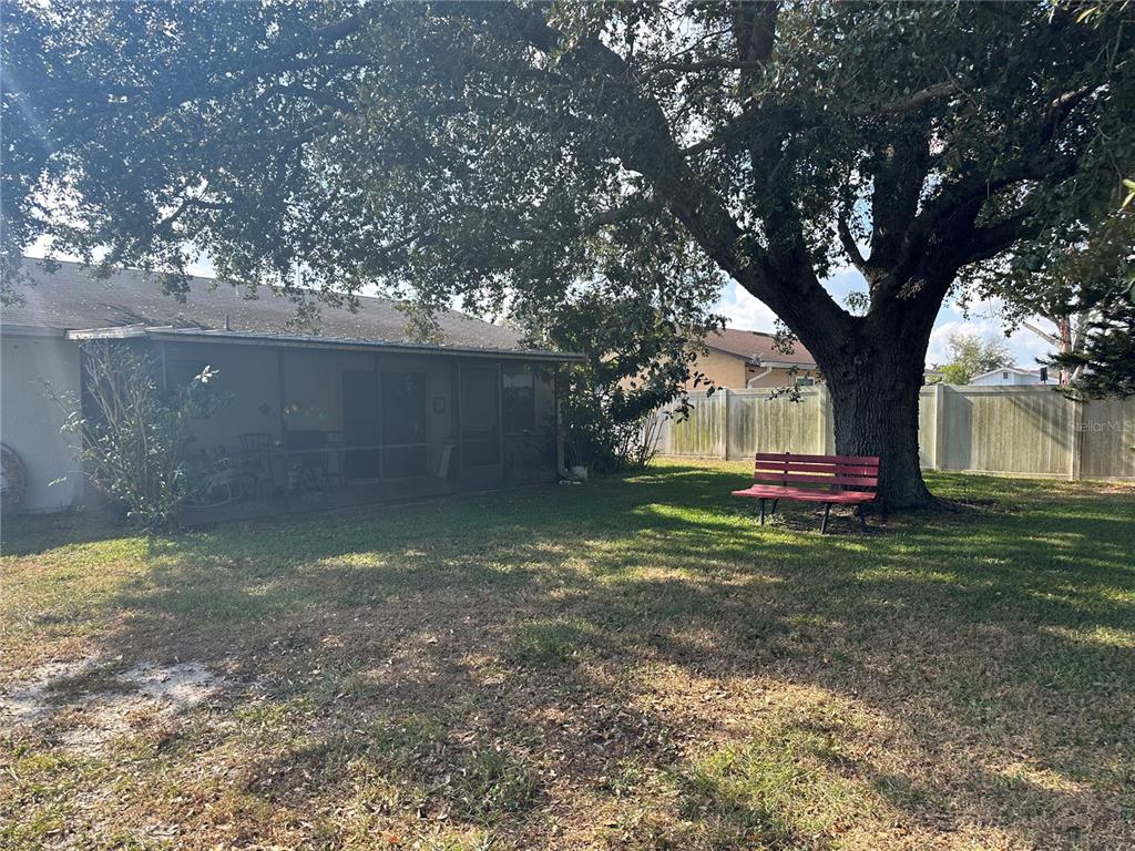 A backyard features a large tree, a red bench, and a screened-in porch — 746 MADERIA COURT, KISSIMMEE, FL