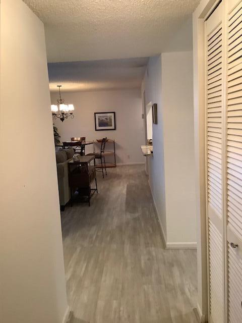 A hallway with light wood-look flooring leads to a dining area with a chandelier — 450 Egret Circle # 9209, Delray Beach FL 33444, DELRAY BEACH, FL