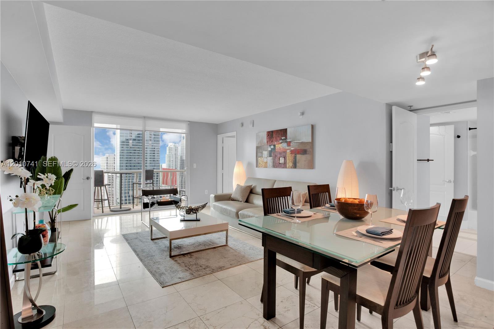 A bright living and dining area features tile floors, modern furniture, and a balcony view — 1200 Brickell Bay Dr # 3515, Miami FL 33131, MIAMI, FL