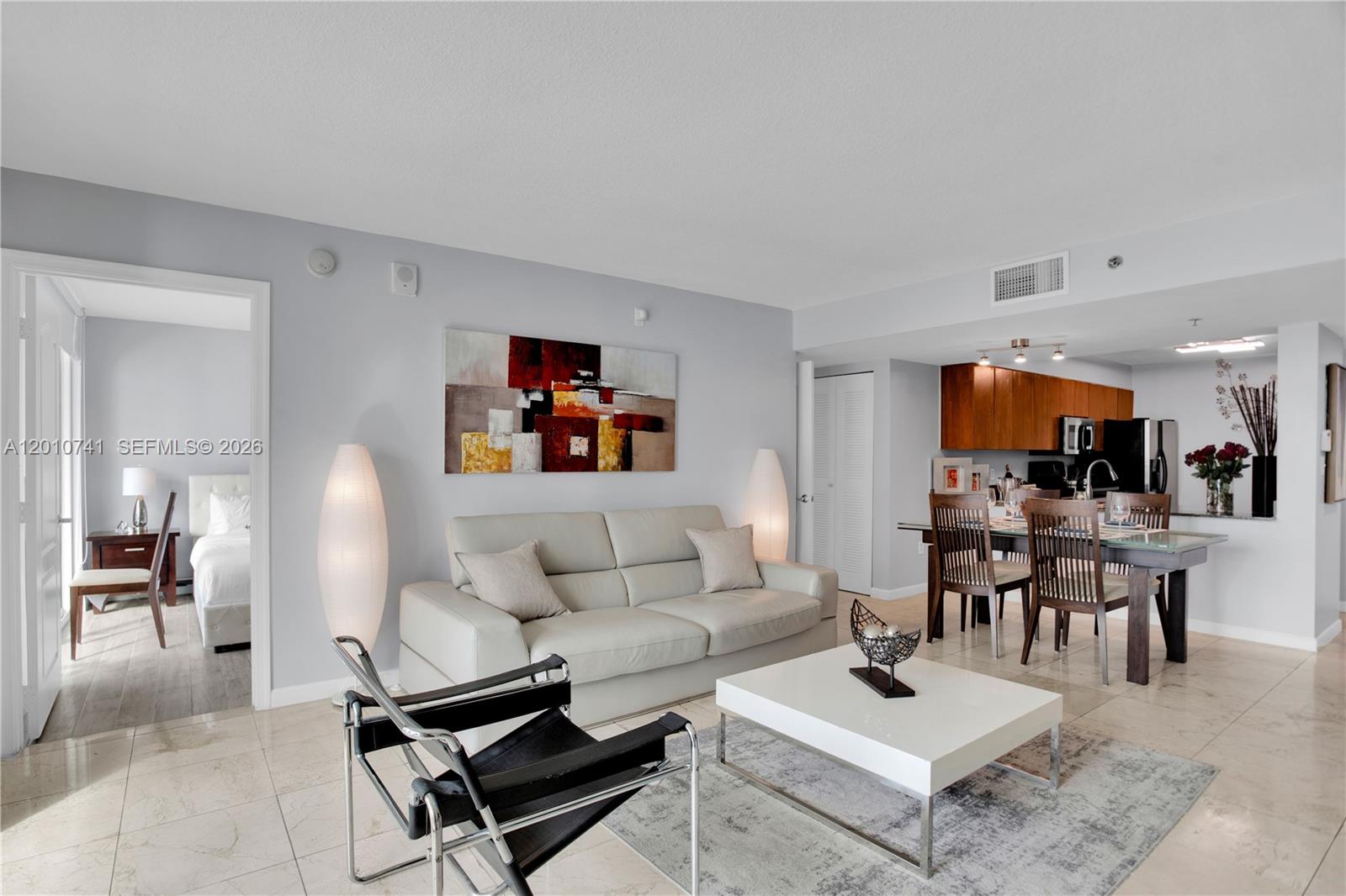 A living room features a white sofa, a black lounge chair, and an adjacent dining area — 1200 Brickell Bay Dr # 3515, Miami FL 33131, MIAMI, FL