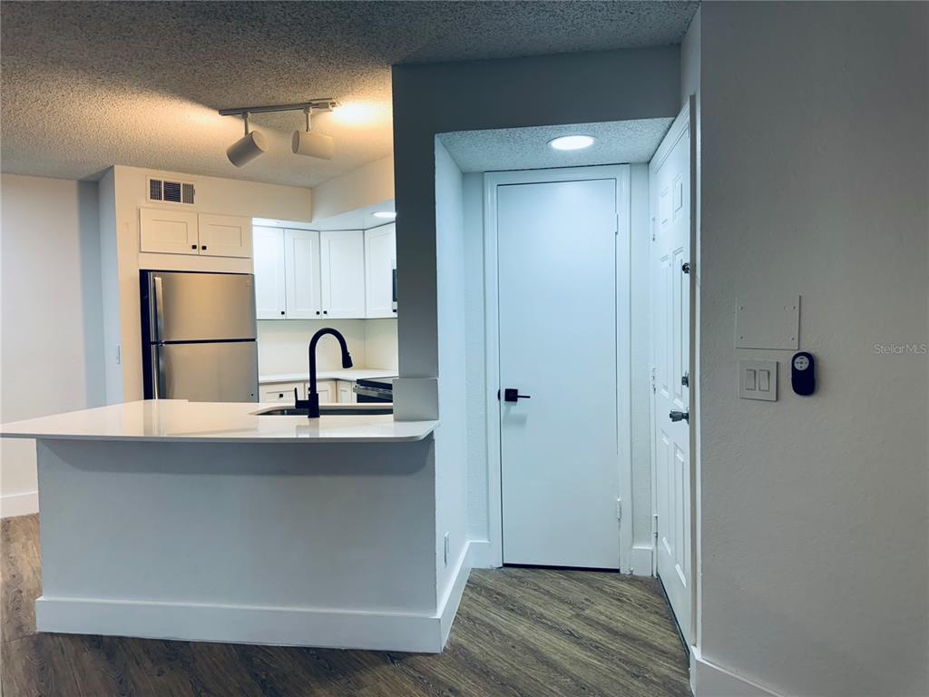A kitchen with white cabinets and a breakfast bar sits next to an entryway door — 4630 COMMANDER DRIVE UNIT 1023, ORLANDO, FL