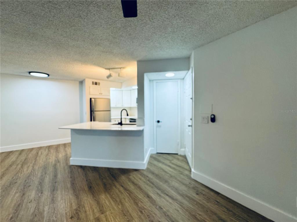A kitchen with a breakfast bar, white cabinets, and wood-look flooring opens to a living area — 4630 COMMANDER DRIVE UNIT 1023, ORLANDO, FL