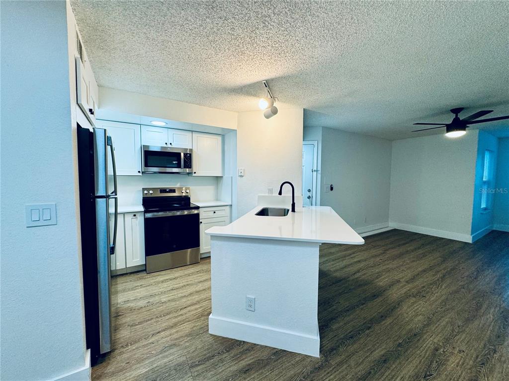 A kitchen features white cabinets, stainless steel appliances, a white island, and wood-look flooring — 4630 COMMANDER DRIVE UNIT 1023, ORLANDO, FL