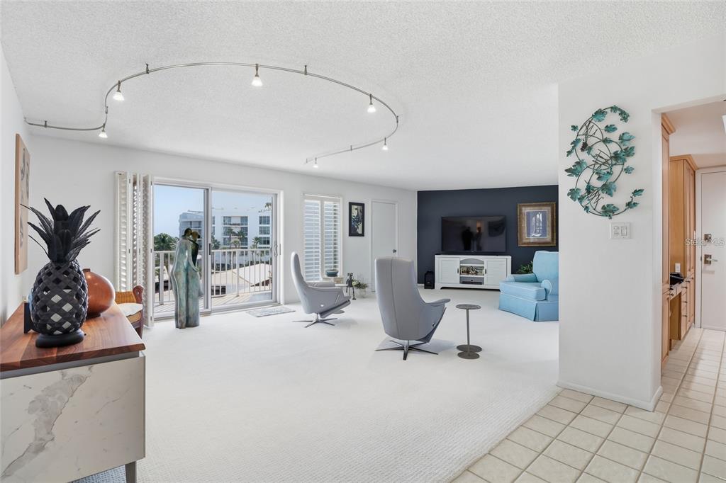 A spacious living room features white carpet, track lighting, and a sliding glass balcony door — 2301 GULF OF MEXICO DRIVE UNIT 45N, LONGBOAT KEY, FL