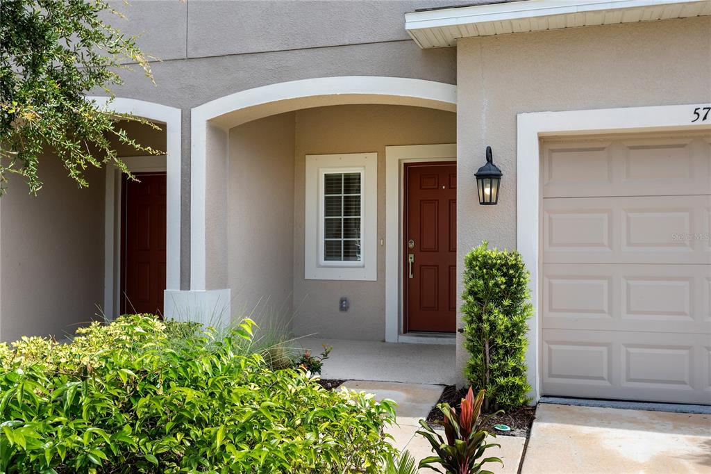 A tan townhouse exterior features a red front door, a garage, and a small garden — 5780 HAVEN TERRACE, NOKOMIS, FL
