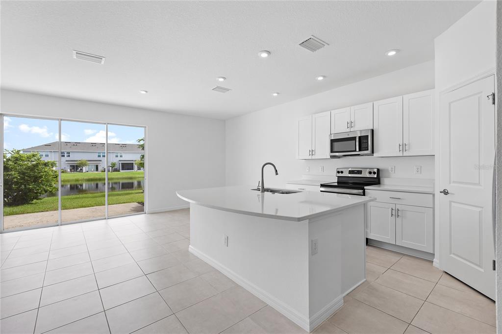 A modern kitchen features white cabinets, a central island, and sliding glass doors to outdoors — 5780 HAVEN TERRACE, NOKOMIS, FL