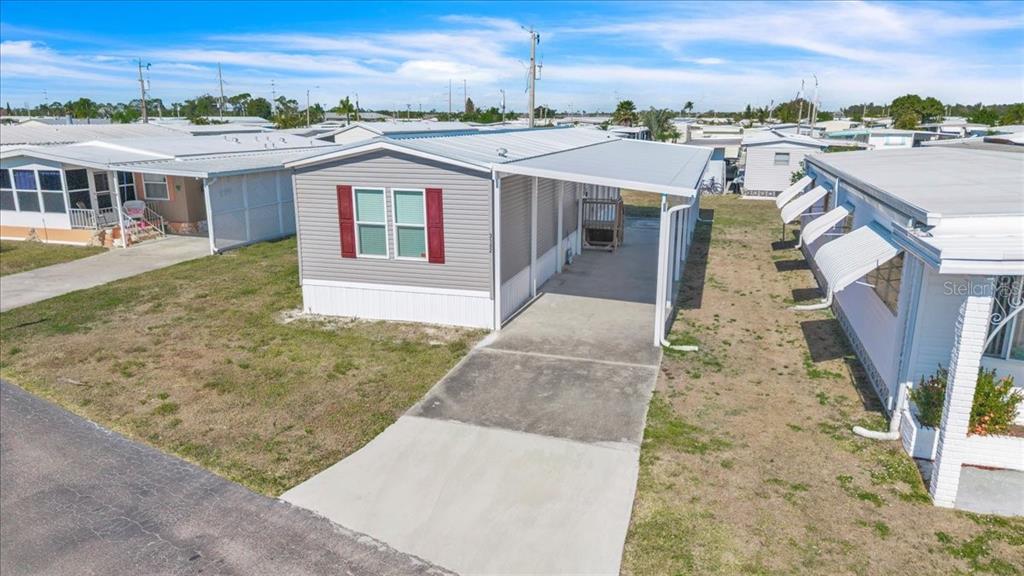 A gray mobile home with red shutters and a concrete carport sits on a lot — 3162 MERCURY LANE, NORTH FORT MYERS, FL
