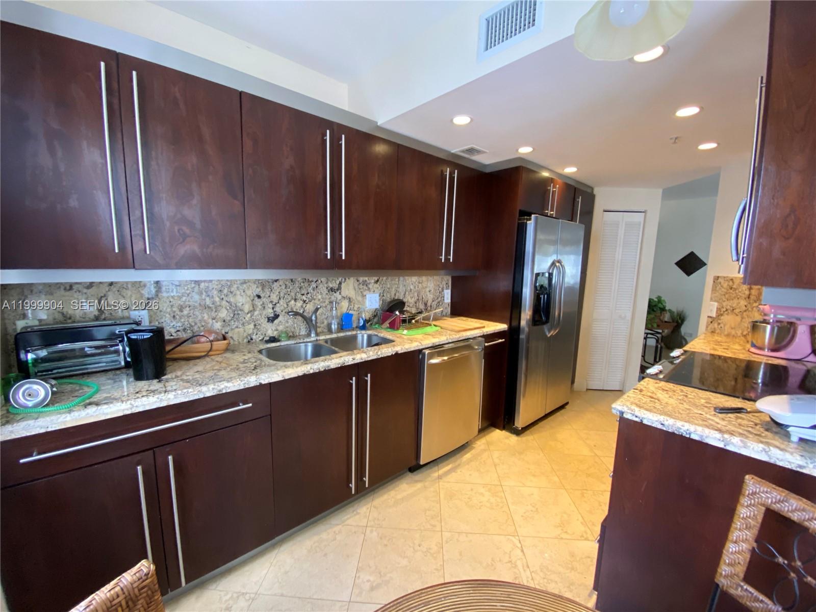 A kitchen features dark wood cabinets, granite countertops, stainless steel appliances, and tile flooring — 701 Brickell Key Blvd # 2104, Miami FL 33131, MIAMI, FL
