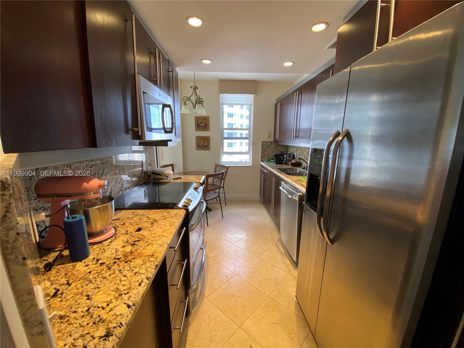 A galley kitchen features dark wood cabinets, granite countertops, stainless steel appliances, and tile flooring — 701 Brickell Key Blvd # 2104, Miami FL 33131, MIAMI, FL