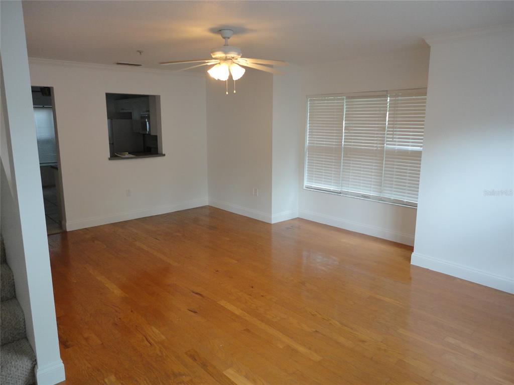 An empty living room features hardwood floors, a ceiling fan, and a kitchen pass-through window — 2636 SW 35TH PLACE UNIT 8, GAINESVILLE, FL