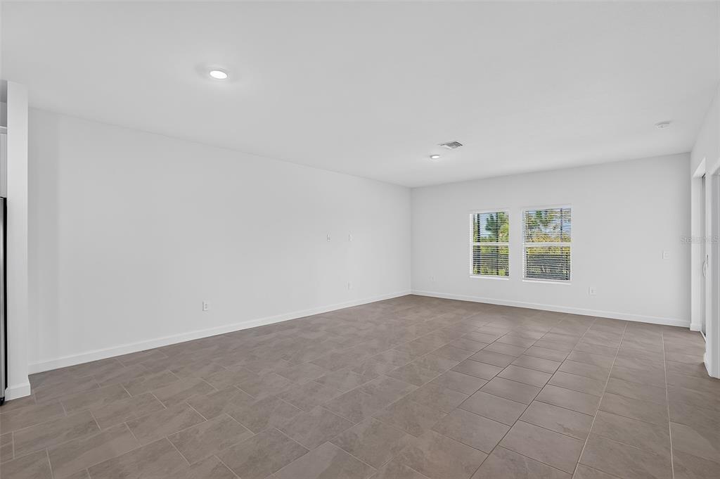 An empty living room features light gray walls, large rectangular floor tiles, and two windows — 13302 GRASSMERE COURT, PUNTA GORDA, FL
