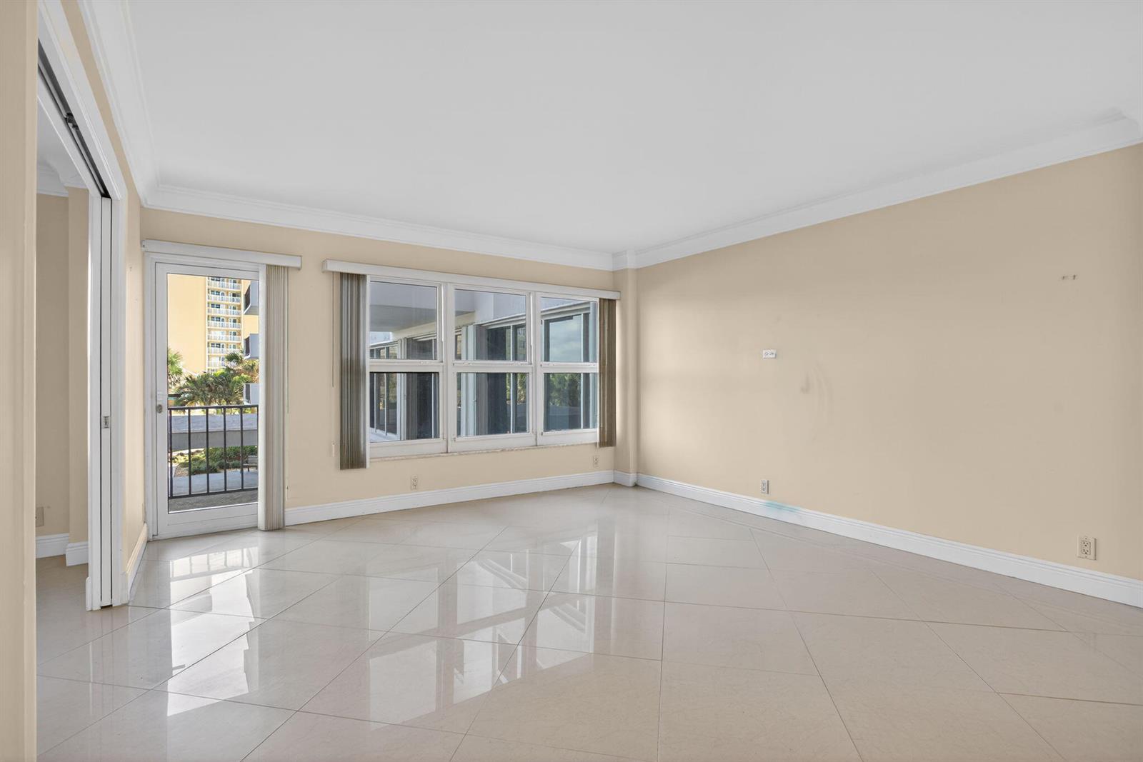 An empty room with beige walls, large windows, tile flooring, and a glass balcony door — 405 N Ocean Boulevard # 208, Pompano Beach FL 33062, POMPANO BEACH, FL