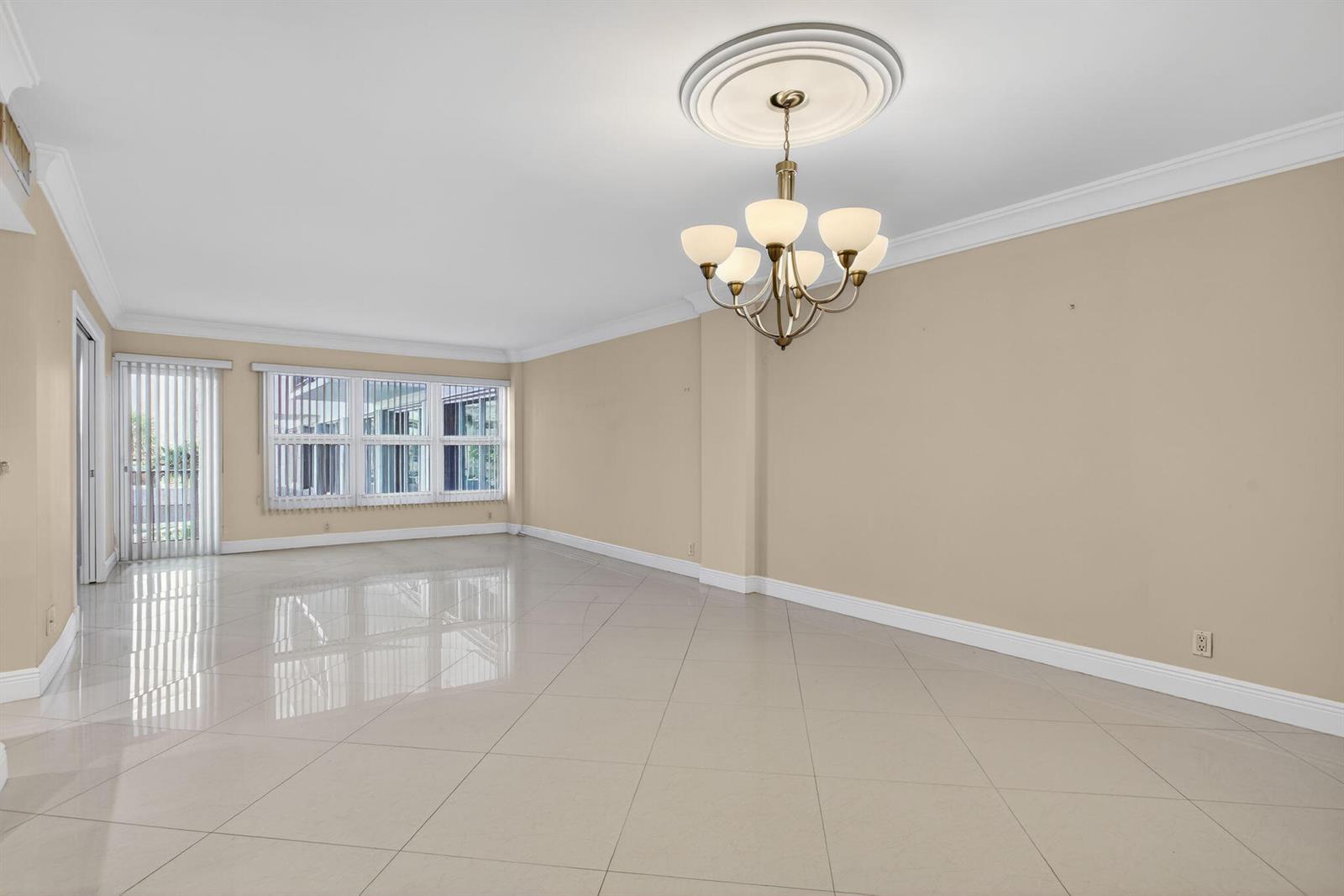 An empty room features beige walls, white crown molding, a chandelier, and glossy tiled floors — 405 N Ocean Boulevard # 208, Pompano Beach FL 33062, POMPANO BEACH, FL