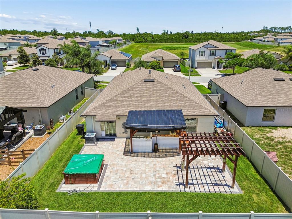 An aerial view of a backyard featuring a paved patio, hot tub, and wooden pergola — 6388 SPIDER LILY WAY, NEW PORT RICHEY, FL
