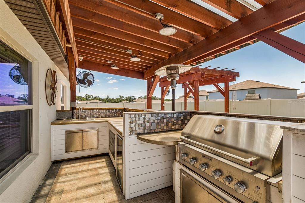 An outdoor kitchen features a stainless steel grill, tiled backsplash, and a wooden pergola roof — 6388 SPIDER LILY WAY, NEW PORT RICHEY, FL