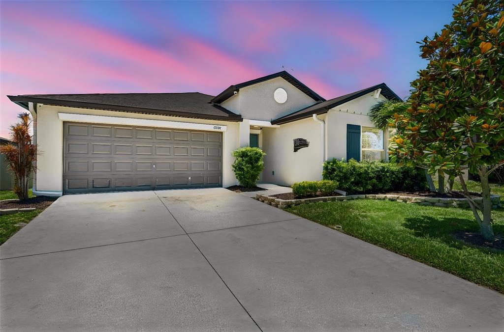 A single-story house with a gray garage door, white stucco exterior, and a concrete driveway — 6388 SPIDER LILY WAY, NEW PORT RICHEY, FL