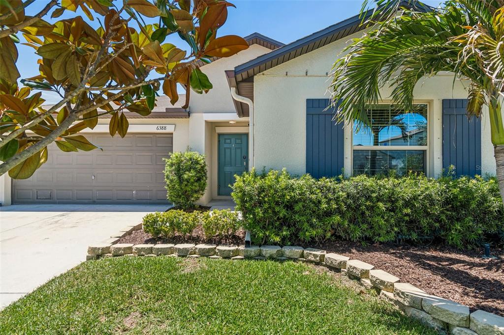 A single-story house exterior features a garage, a teal front door, and blue window shutters — 6388 SPIDER LILY WAY, NEW PORT RICHEY, FL