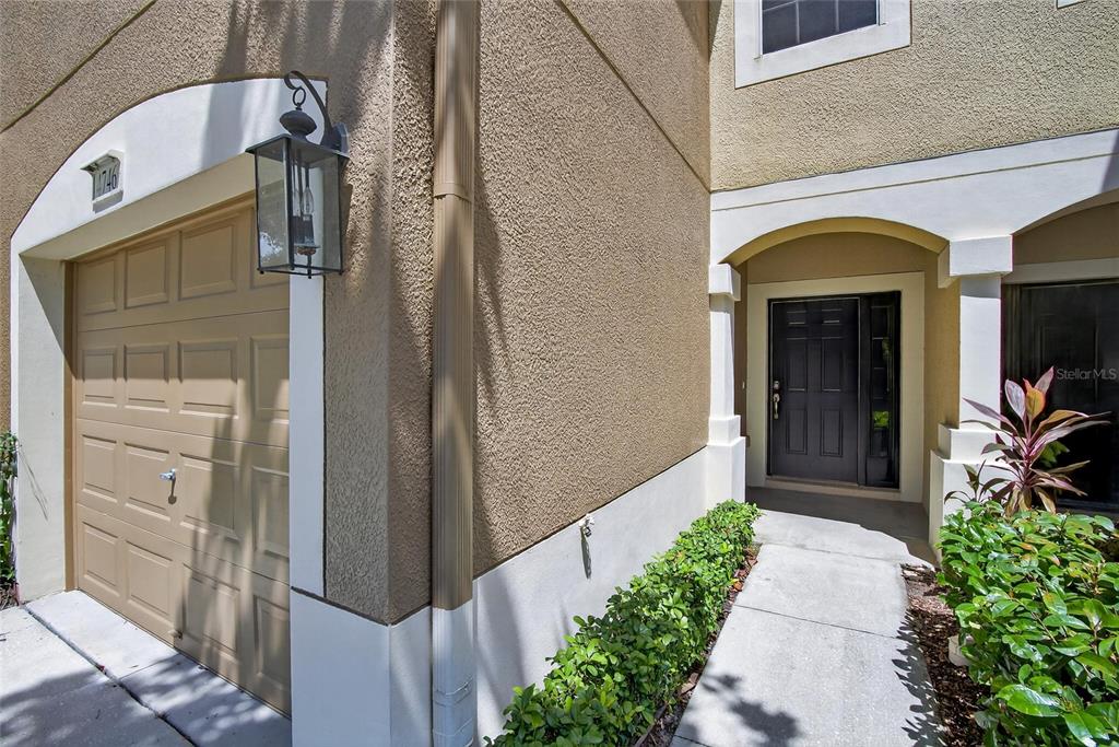 A tan stucco townhouse exterior features a garage, a dark front door, and landscaping — 4746 POND RIDGE DRIVE, RIVERVIEW, FL