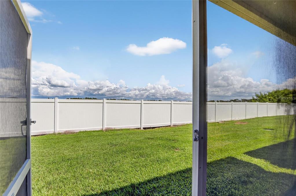 A view of a grassy backyard enclosed by a white vinyl fence from a doorway — 4746 POND RIDGE DRIVE, RIVERVIEW, FL