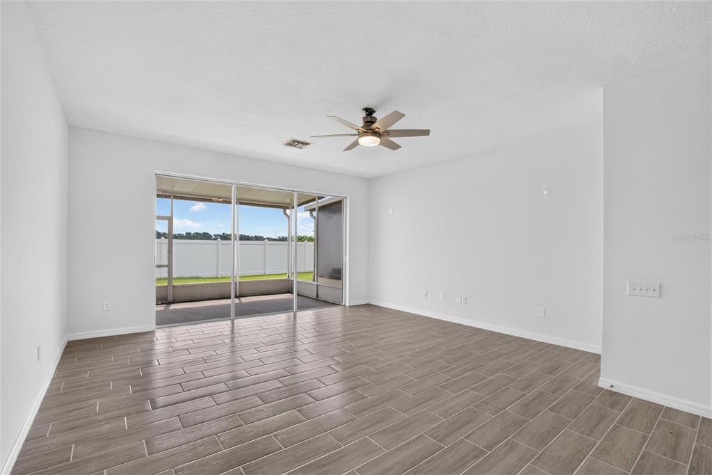 An empty living room with wood-look tile flooring, a ceiling fan, and sliding glass doors — 4746 POND RIDGE DRIVE, RIVERVIEW, FL