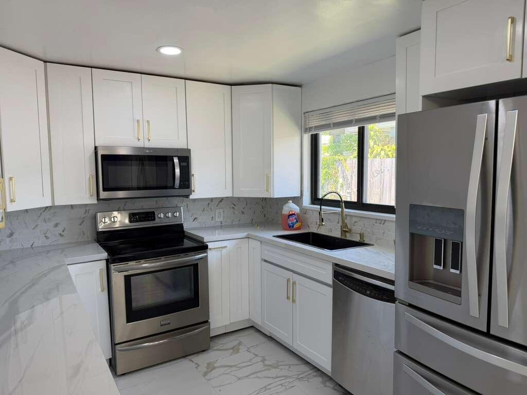 A kitchen with white cabinets, stainless steel appliances, marble-look countertops, and a black sink — 160 SE 15th Avenue Unit A, Pompano Beach FL 33060, POMPANO BEACH, FL