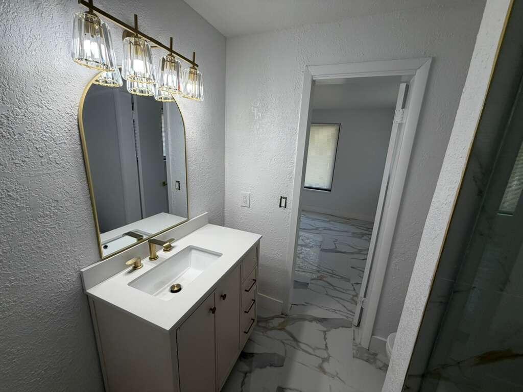 A bathroom features a white vanity, gold faucet, arched mirror, and marble-look tile flooring — 160 SE 15th Avenue Unit A, Pompano Beach FL 33060, POMPANO BEACH, FL