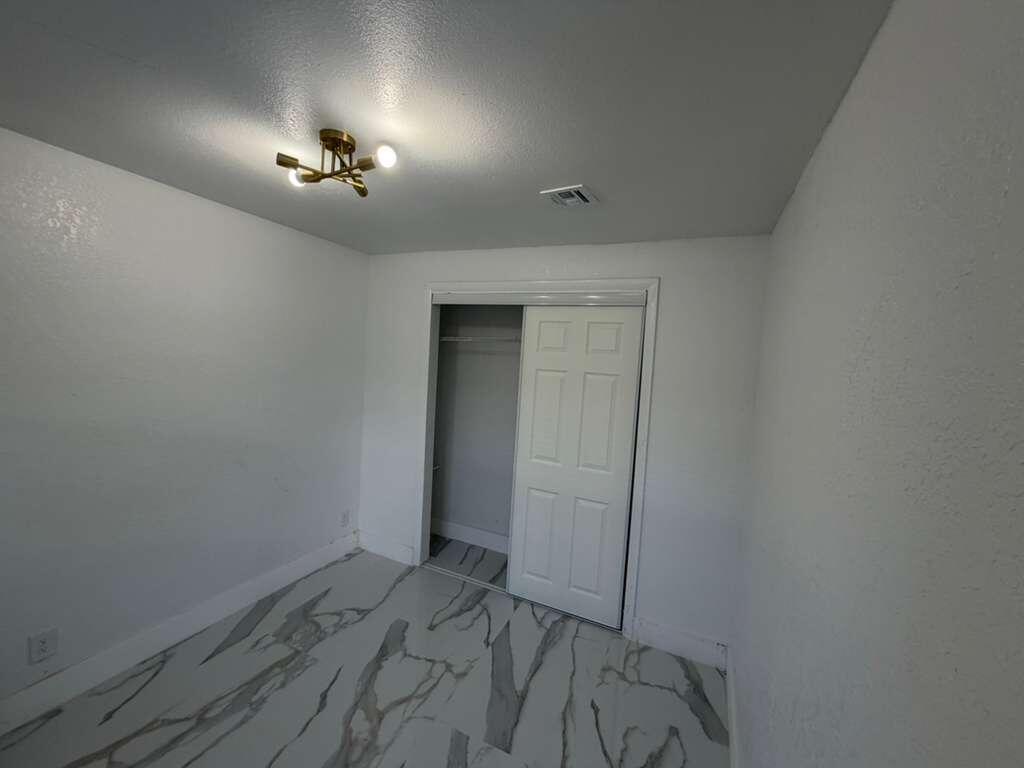 A small bedroom features white walls, a modern gold light fixture, and marble-patterned tile flooring — 160 SE 15th Avenue Unit A, Pompano Beach FL 33060, POMPANO BEACH, FL