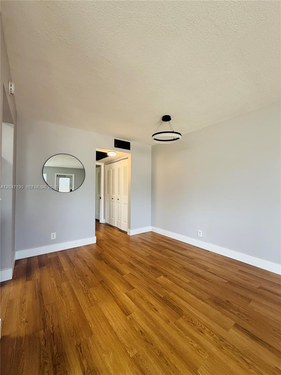 An empty room features light gray walls, wood-look flooring, a circular mirror, and a modern light — 21 Windsor B # b, West Palm Beach FL 33417, WEST PALM BEACH, FL
