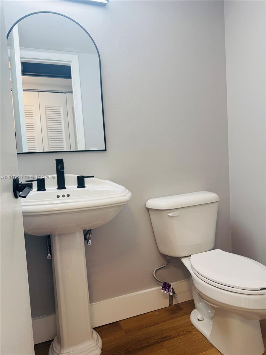 A bathroom features a white pedestal sink, a toilet, and an arched mirror on gray walls — 21 Windsor B # b, West Palm Beach FL 33417, WEST PALM BEACH, FL