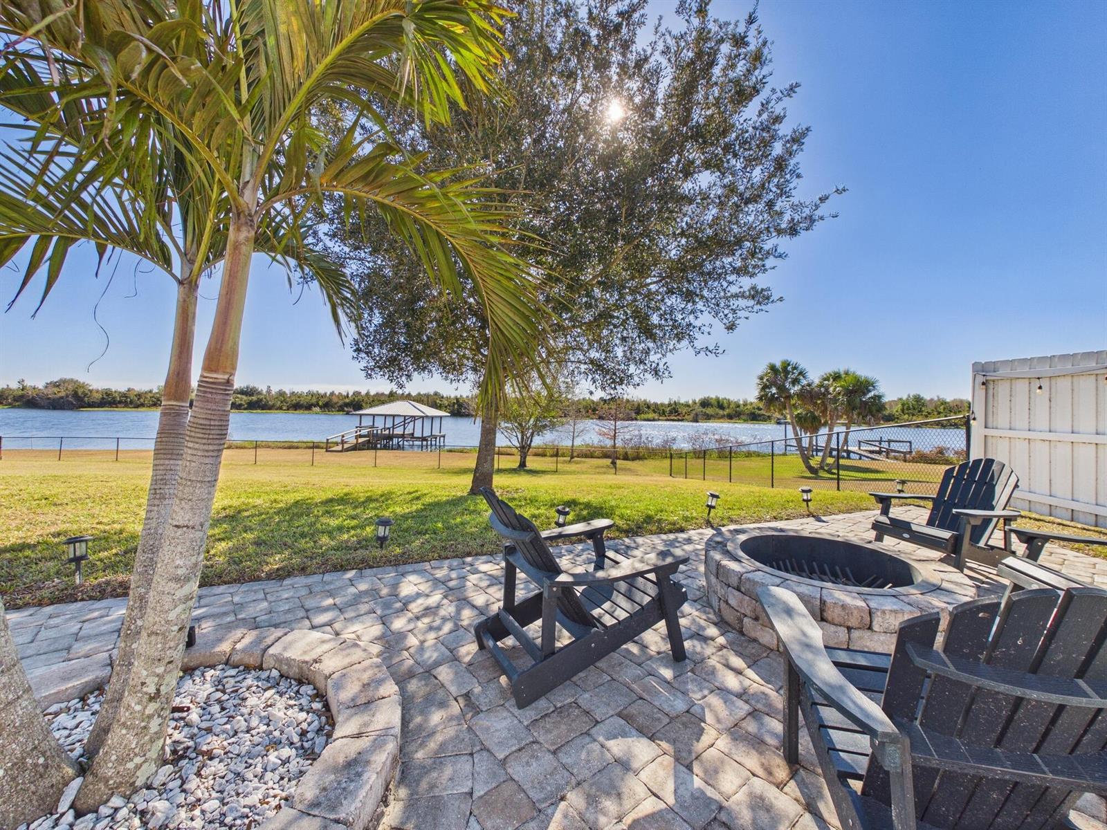 A stone patio with a fire pit and chairs overlooks a lake and dock — 14216 SW 144th Parkway, Okeechobee FL 34974, OKEECHOBEE, FL