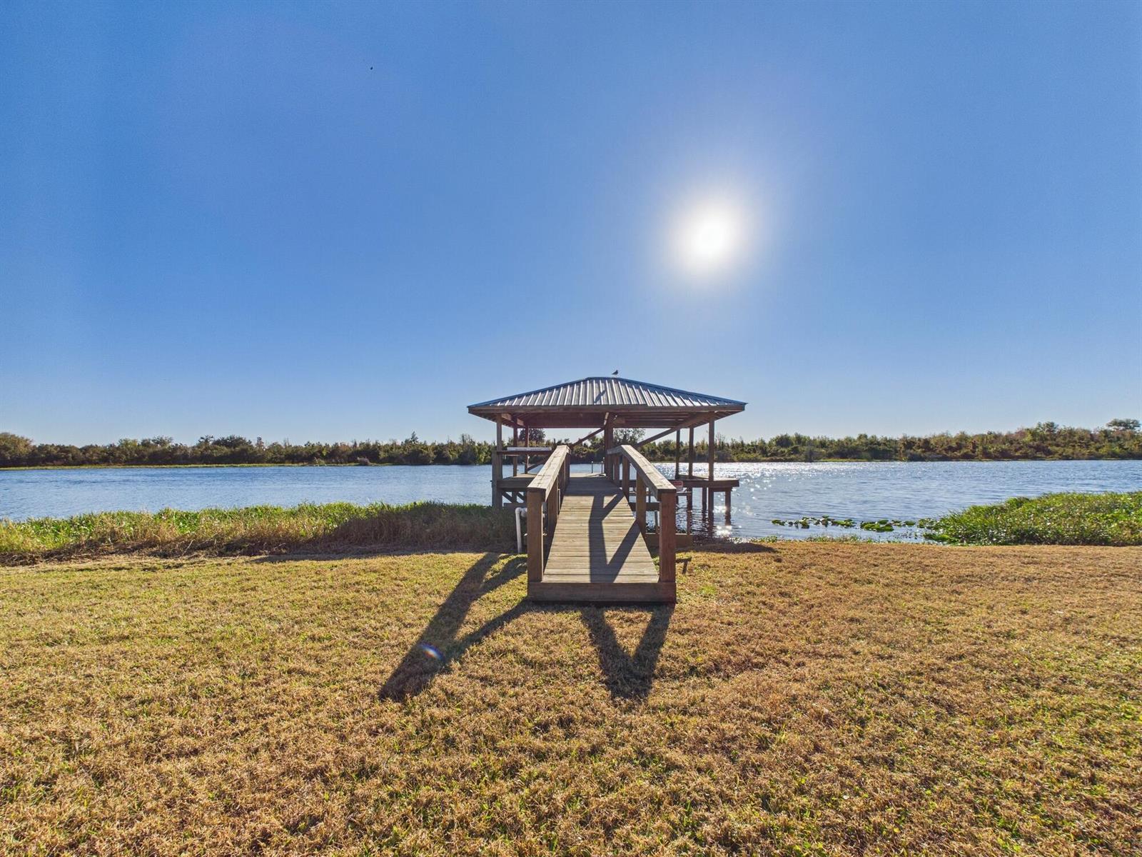 A wooden boat dock with a metal roof extends into a lake from a grassy yard — 14216 SW 144th Parkway, Okeechobee FL 34974, OKEECHOBEE, FL
