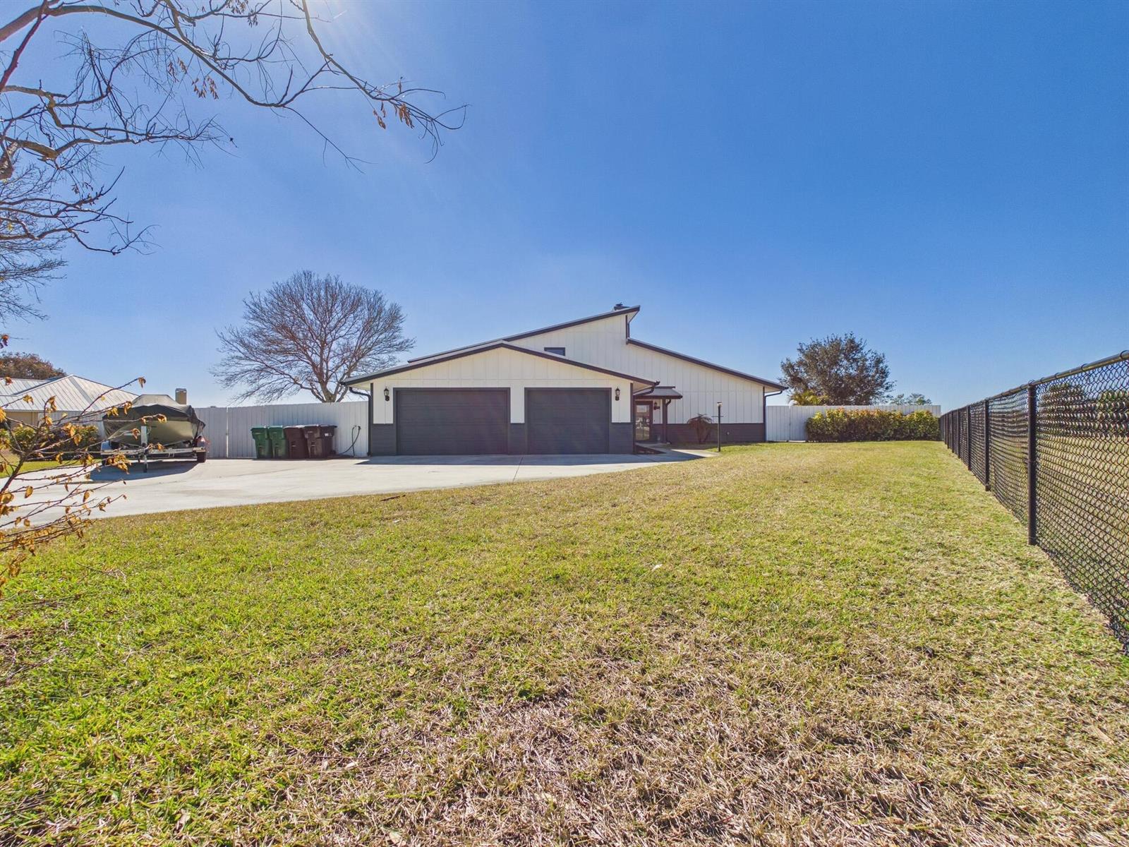 A single-story house with a two-car garage and a large grassy yard under a clear sky — 14216 SW 144th Parkway, Okeechobee FL 34974, OKEECHOBEE, FL