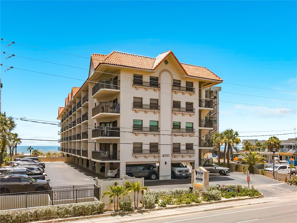 A multi-story apartment building with a tiled roof, balconies, and ground-level parking — 4000 GULF BOULEVARD UNIT 203, ST PETE BEACH, FL