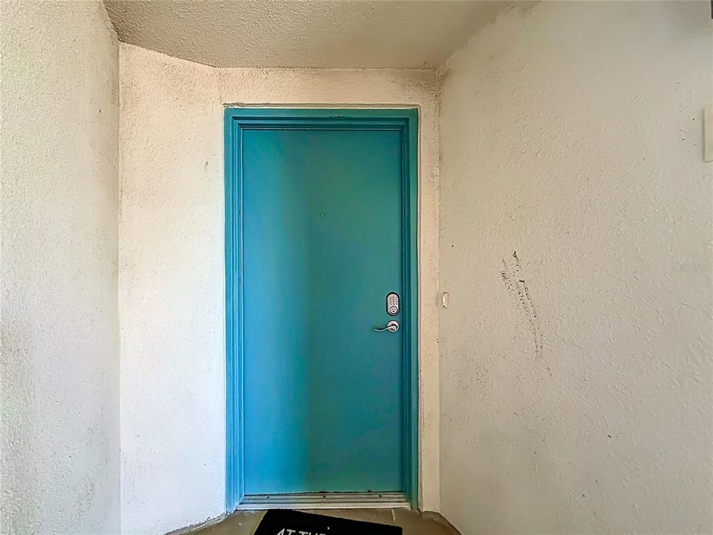 A bright blue front door is set into a white stucco wall — 4000 GULF BOULEVARD UNIT 203, ST PETE BEACH, FL