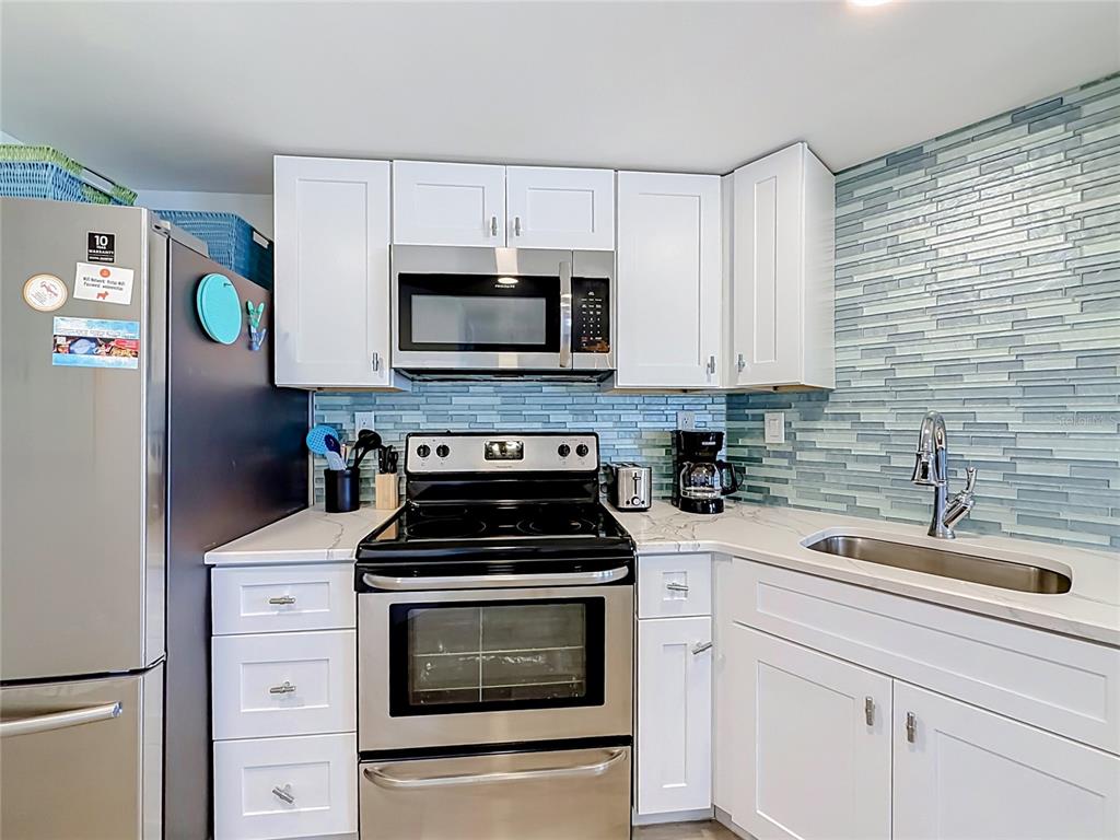 A kitchen features white cabinets, stainless steel appliances, and a blue glass tile backsplash — 4000 GULF BOULEVARD UNIT 203, ST PETE BEACH, FL