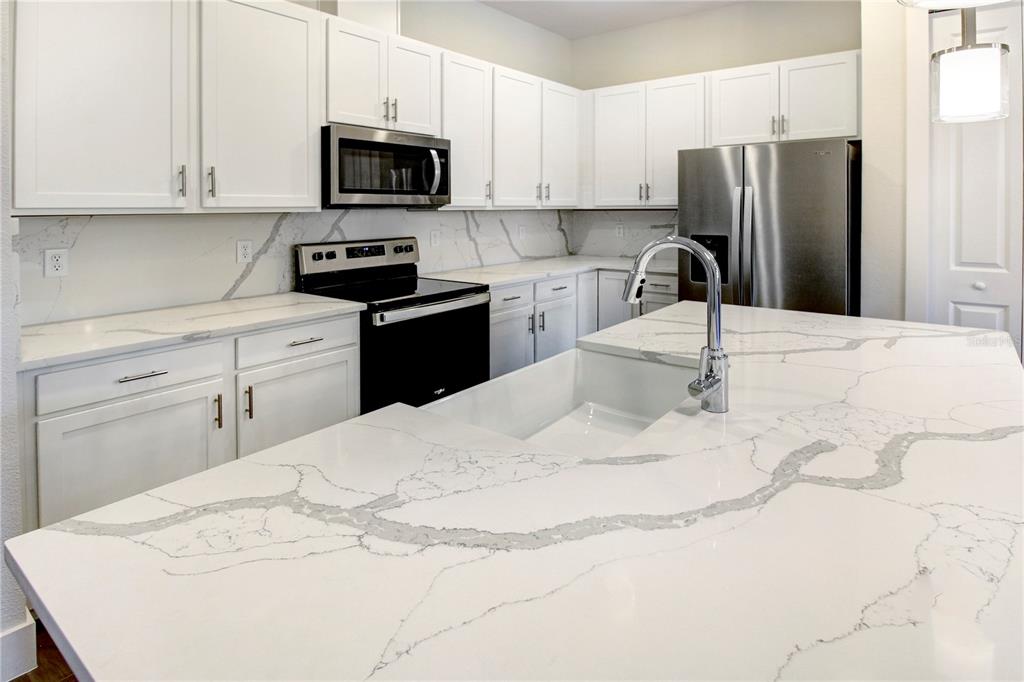 A modern kitchen features white cabinets, stainless steel appliances, and a large marble-patterned island — 1519 HERITAGE PLACE, OVIEDO, FL