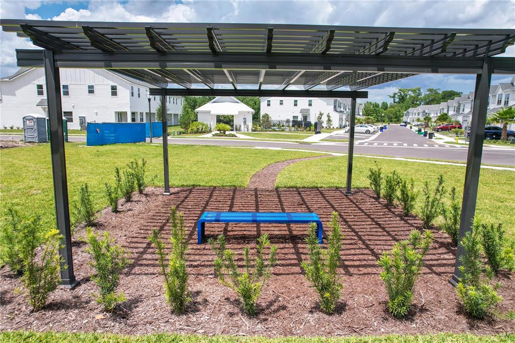 A blue bench sits under a metal pergola in a landscaped residential yard — 1519 HERITAGE PLACE, OVIEDO, FL