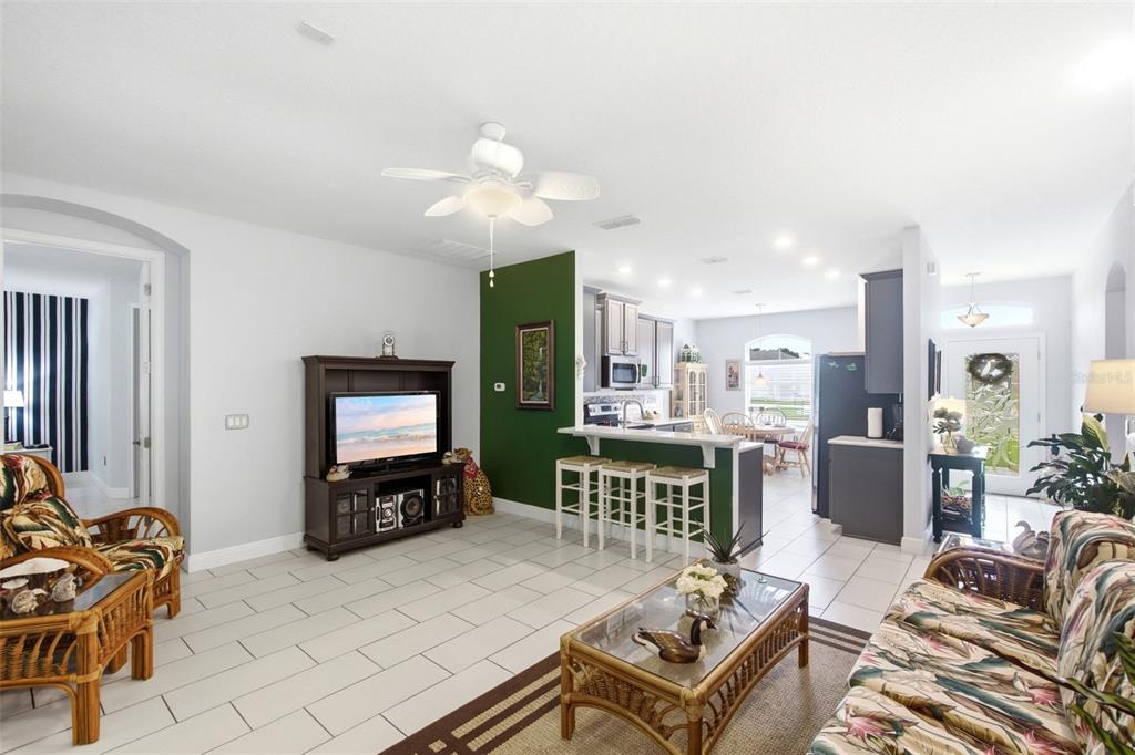 A living room with a green accent wall, wicker furniture, and an open kitchen — 500 BIRD SONG COURT, DELAND, FL