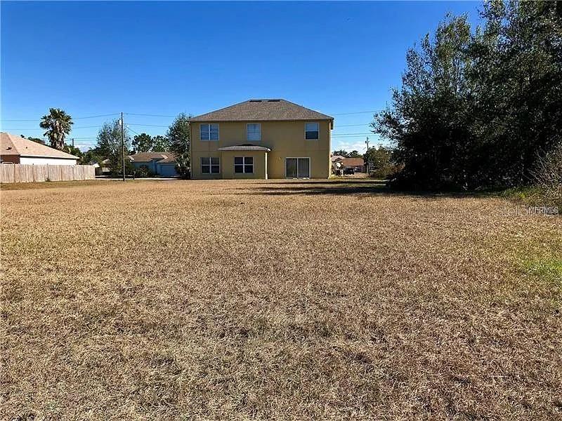 A two-story house stands behind a large, dry, grassy field under a clear blue sky — 546 KILIMANJARO DRIVE, KISSIMMEE, FL