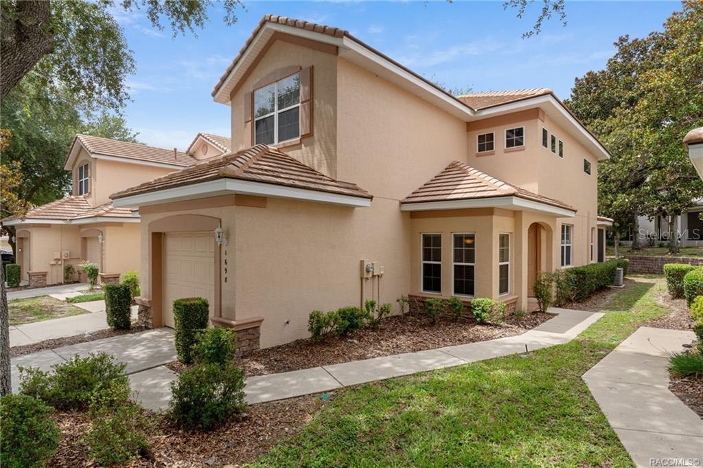 A two-story tan stucco townhouse with a tile roof, single-car garage, and landscaped front yard — 1698 W SPRING MEADOW LOOP, LECANTO, FL
