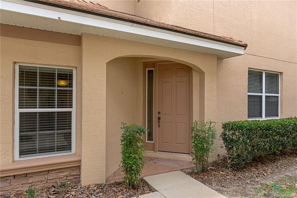 The exterior of a tan stucco house features a covered entryway with a front door — 1698 W SPRING MEADOW LOOP, LECANTO, FL