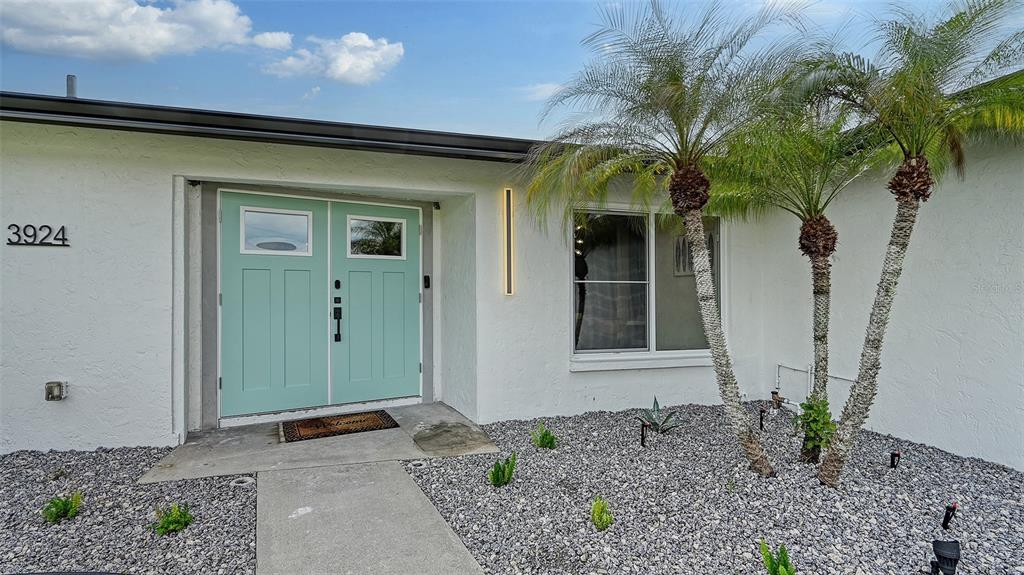 The exterior of a white house features a light blue double door and palm trees — 3924 HELENE STREET, SARASOTA, FL